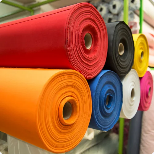 A display of various colored fabric rolls stacked in a store, showcasing a range of textures and patterns.